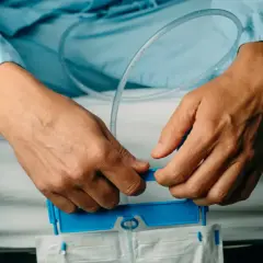 Pacjent w niebieskiej koszuli szpitalnej przygotowuje się do oddawania moczu po wyjęciu cewnika, trzymając worek na mocz.
