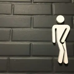 Biały symbol mężczyzny na ciemnej, ceglanej ścianie. Może symbolizować problemy z oddawaniem moczu, takie jak niskie ciśnienie moczu u mężczyzn.