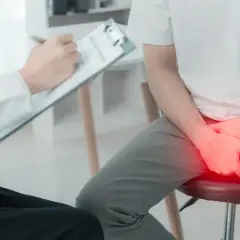 Lekarz spisuje zalecenia po cystoskopii. Pacjent siedzi, trzymając ręce na kroczu, gdzie widoczny jest czerwony obszar bólu.