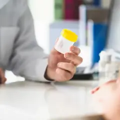 Lekarz podaje pacjentowi pojemnik na badanie moczu, wyjaśniając, jak się przygotować.