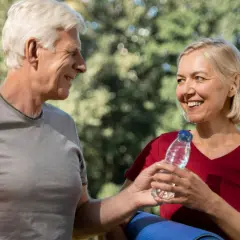Uśmiechnięci seniorzy po treningu. Kobieta podaje mężczyźnie wodę, dbając o jego zdrowie.