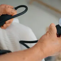 Dłonie seniora mierzą ciśnienie. Aparat z manometrem i pompką w rękach, kontrola zdrowia.