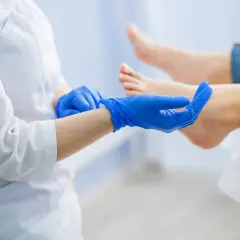 Podolog w niebieskich rękawiczkach bada stopę pacjentki, zastanawiając się, jak długo odrasta paznokieć po urazie.