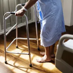 Osoba z chorobą Parkinsona, wspierając się chodzikiem, rozpoczyna proces pielęgnowania.
